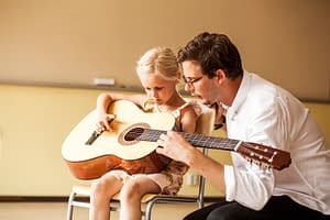 Male teacher teaching girl to play guitar